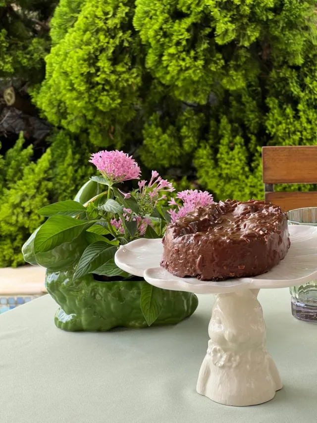 Bolo de brigadeiro sobre suporte de coelho de cerâmica entre flores